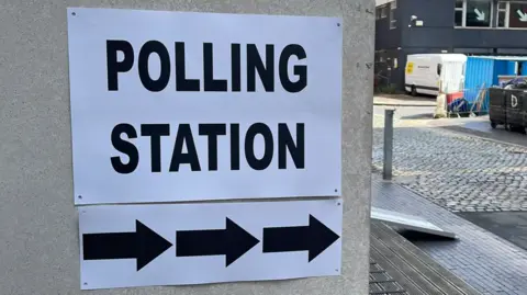 A black and white Polling Station sign stuck to a grey concrete wall