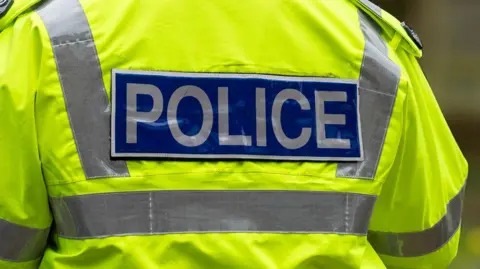 A close-up of the back of a police officer's high-vis yellow jacket. It has the word 'police' across the back. 