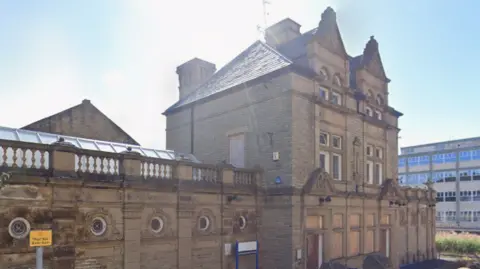 Close-up of a three-storey stone building in Batley. The former leisure centre is boarded up.