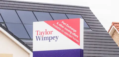 Getty Images Close up of a large sign in front of a newbuild house, saying "Taylor Wimpey"