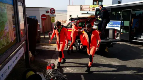 Getty Images Diving firefighters wearing bright orange wetsuits pack their belongings into the back of a car