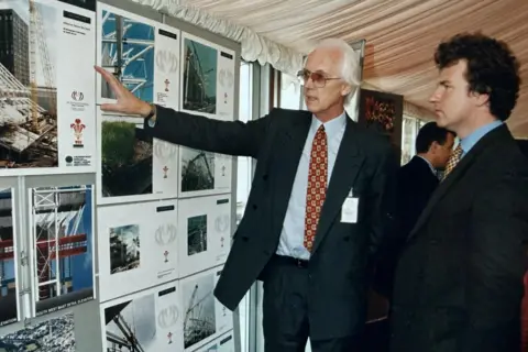 Pat Thompson Archive Suited with collar and tie, Pat stands before a display board showing plans for the stadium to Peter Ainsworth