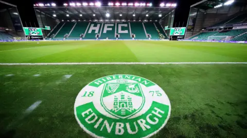 Hibernian's floodlit stadium with a large club logo on the pitch