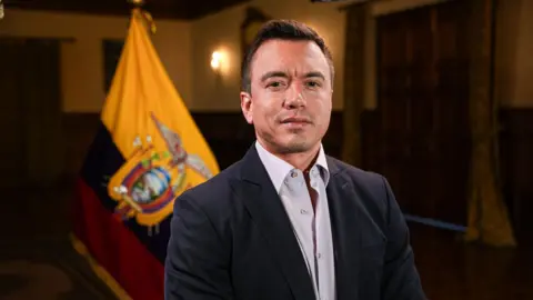 President Noboa looks directly at the camera with the Ecuadorean flag in the background