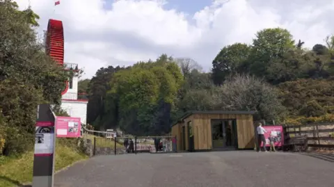 CG Visualisation IOM The Laxey Wheel to the left, trees in the middle, and a square wooden clad building to the right, a mock up of the new entrance.