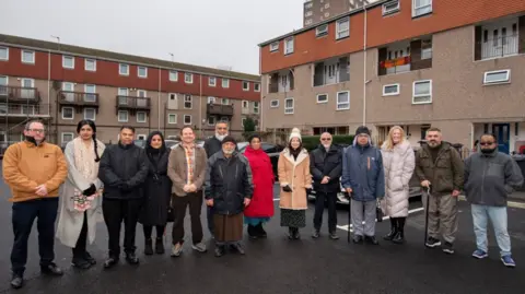 A group of 14 people standing on freshly laid parking spaces 