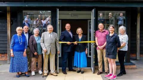 A group of people standing around the entrance to a village hall with two people at the centre cutting a ribbon