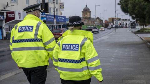 A male and female police officer walking together down a high street