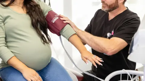A pregnant woman wearing a green long-sleeve top getting her blood pressure taken.