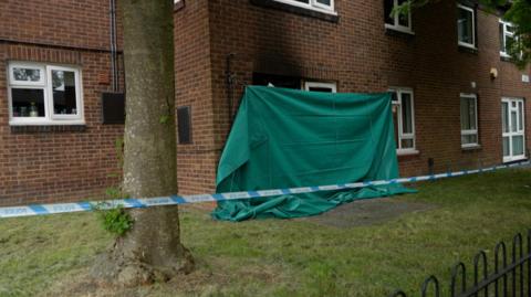 Green sheet covering the door of a flat which was on fire, with a police cordon around the property too