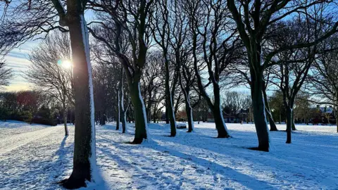 BBC Weather Watchers/ Mark1972 Snow blankets path and trees in Blyth in Northumberland, with foot steps visible.