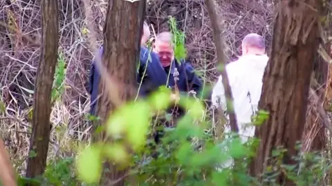 Police Hungary Three men, two in blue overalls and one in white, search a woodland