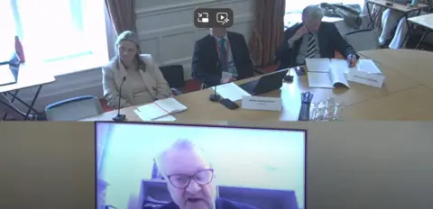 Government of Jersey Prof Hugo Mascie-Taylor shown on a video screen with a panel of three in the background