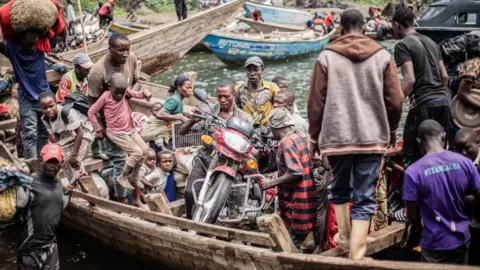 AFP Displaced Congolese people flee the area of Minova by boat. The small, wooden boat is packed and one man has even loaded his motorbike onto the vessel.