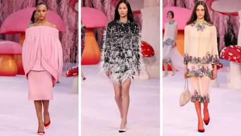 Getty Images Three models on a Chanel catwalk - one wears a pale pink suit with an off-the-shoulder top with draped cape shoulder detail, one has a feathered black and white dress and the third a sheer embroidered suit 