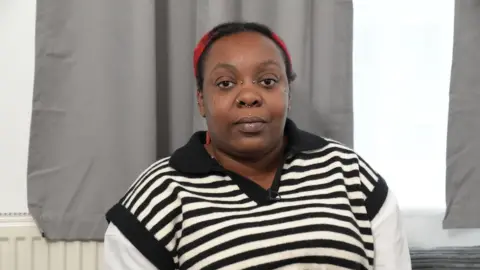 A head and shoulders picture of a woman with several face piercings, wearing a black and white stripy top.