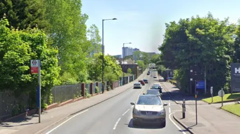 A street view of Icknield Port Road with trees lining each side of the road and cars driving by.