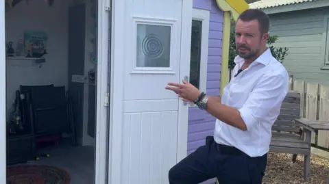 Estate agent Simon Mitchell pointing at a purple beach hut with its door open