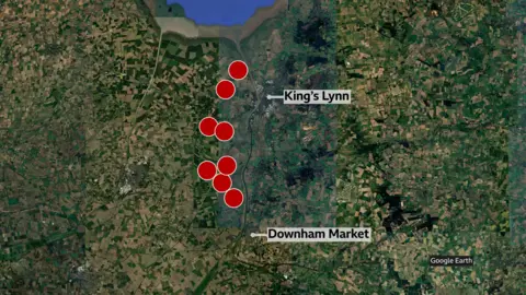 BBC/Google Satellite map showing a rural area between King’s Lynn and Downham Market. Multiple red circular markers are arranged in clusters across farmland and waterways. Labels identify both towns, and a Google Earth credit appears in the lower-right corner.