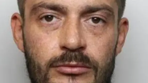 South Yorkshire Police Thomas Hampton, a man with a black beard and black hair, with dark brown eyes, in his mugshot