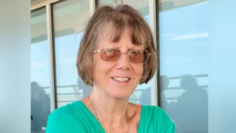 Suffolk Police Christine Murton is in the middle of the image looking towards the camera. She has short brown hair and is wearing glasses and a green T-shirt. 