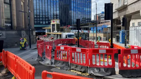 BBC/NATHAN TURVEY A picture of Leeds railway station with roadworks in the foreground and tha station in the background, twith the clock tower and a building in the background.