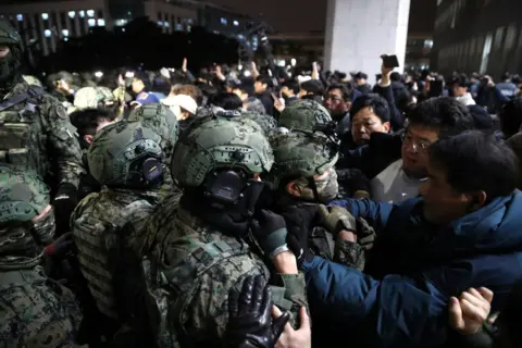 Getty Images Soldiers wearing helmets and camouflage outfits clash with crowds of civilians during the night
