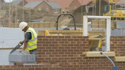 New build houses on a development under construction. A worker is using a saw.