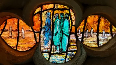 St John's Church A close-up of a pane of the glass in a flower shape with several biblical figures depicted in hues of orange, turquoise and blue