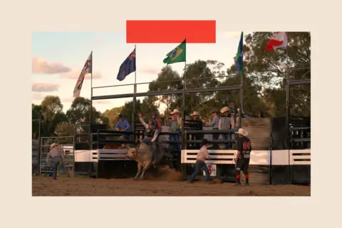 A rider holds on as a bull in front of a rodeo crowd