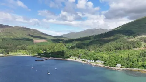 An aerial view of Inverie's white walled properties next to the sea and a below tree covered hill