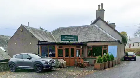 A small village pub and restaurant with a car parked outside and grey sky above