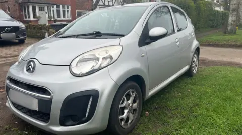 Silver Citroen C1 in front of house.