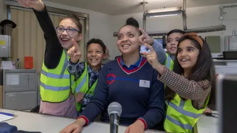 Four children gathered around a Transport for London staff member, all smiling together in an office