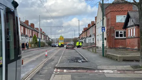 Red and white tape blocks a tram line while workers are on scene to repair overhead lines
