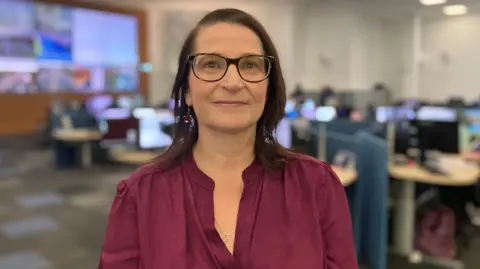 Sam Read/BBC The East region's head of service delivery, Heather Openshaw, is looking straight at the camera and smiling with a closed mouth. She has brown-rimmed glasses and is wearing a V-necked maroon top.