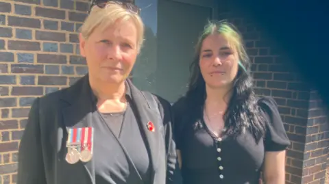 A woman wearing a black dress and jacket with military medals and a young woman in a black dress