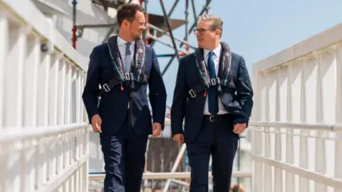 Stephen Morgan Stephen Morgan and Sir Keir Starmer are dressed in suits and are walking along a jetty with life vests on.