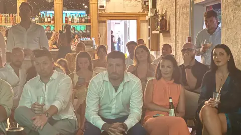 People sat on chairs looking at a screen and concentrating.