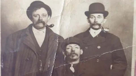 Athelstan Museum Three men stood with pipes and flat caps in a black and white photo.