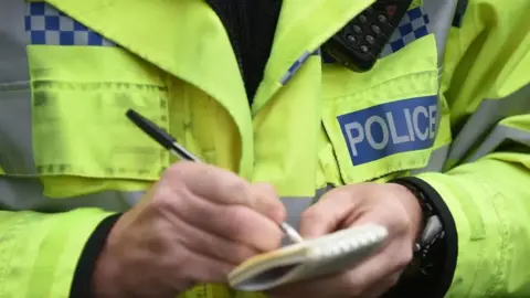 Close up of police officer writing in notebook wearing yellow hi vis jacket