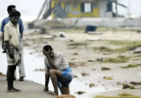 Indian men stand exhausetd after searching for missing relatives at Silver Beach in Cuddalore, some 185 kms south of Madras, 27 December 2004, after tidal waves hit the region. 