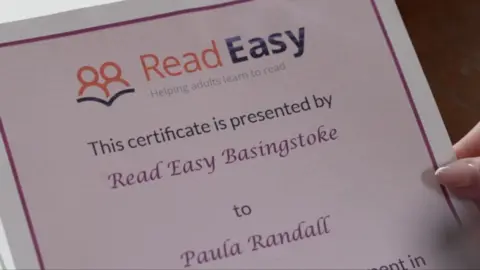 Pictured is part of a paper certificate being held by a woman. The certificate is from an organisation called Read Easy Basingstoke, and it says its being presented to Paula Randall.