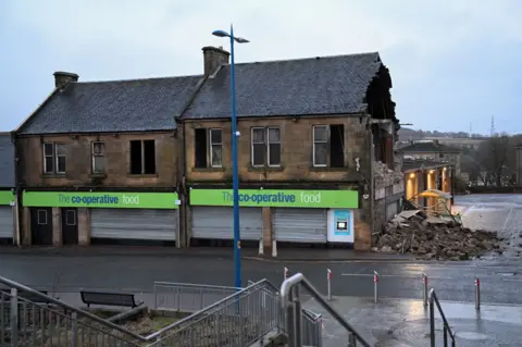 PA Media The Co-Op in Denny near Falkirk viewed from the front is missing a whole stone wall on the right. The rubble is strewn across the road. 