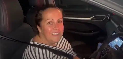 Woman wearing white and black top sitting in car.