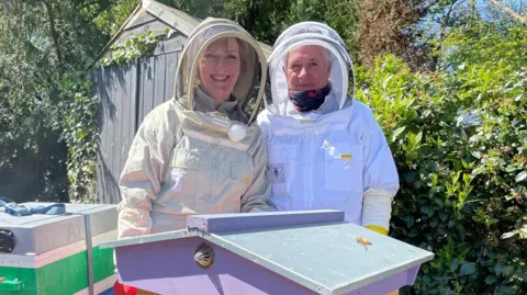 BBC Two people in beekeeping gear standing by a bee hive
