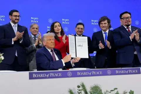 Getty Images U.S. President Donald Trump holds up his signature on the founding charter as Shaikh Isa bin Salman bin Hamad Al Khalifa, Bahrain's Minister of the Prime Minister's Court (L), Prime Minister of Pakistan Shehbaz Sharif (2nd L), President of Kosovo Vjosa Osmani (4th L), Morocco's Foreign Minister Nasser Bourita (3rd R), President of Argentina Javier Milei (2nd R) and Prime Minister of Mongolia Gombojavyn Zandanshatar (R) look on during a signing ceremony for the “Board of Peace”. 