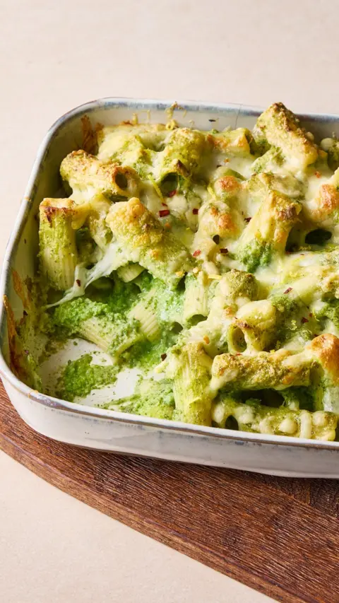 A white roasting tin containing pasta in a green sauce. A portion has been taken out.