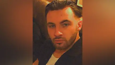 Contributed What appears to be a selfie of Chas Corrigan's face. He has slicked-back hear and a full, short beard. He is sitting on padded seating. He is wearing a black short-sleeved shirt over a white T-shirt 