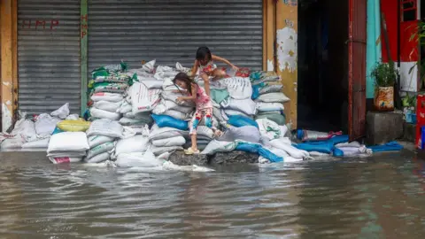 Getty Image Two girls play atop sand bags that are placed outside a shop, at a flooded part of the coastal town of Tondo, where the poorest of the poor in the Philippines reside in